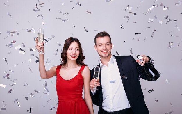 Man in pak en vrouw in rode jurk met champagneglazen geïsoleerd op een grijze achtergrond met confetti