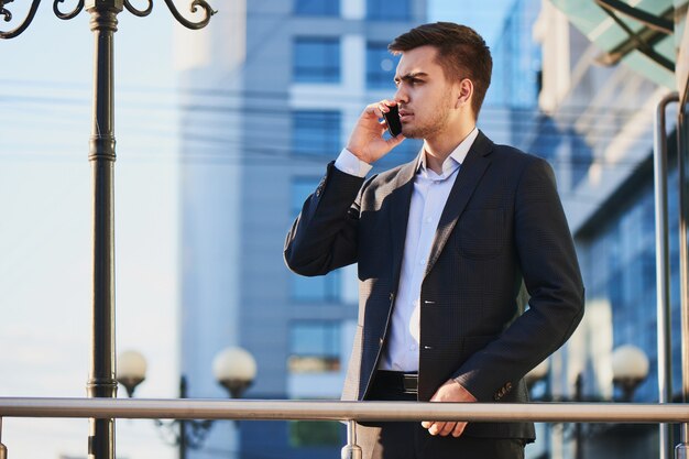 Man in pak praten op mobiele telefoon tegen het gebouw met een glazen gevel