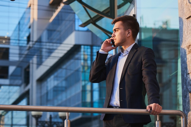 Man in pak praten op mobiele telefoon tegen het gebouw met een glazen gevel