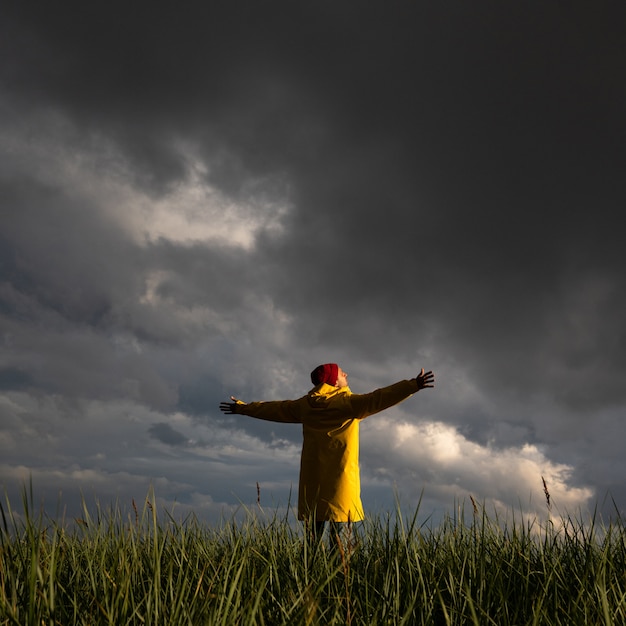 Man in regenjas spreidende handen wijd open staande op het veld