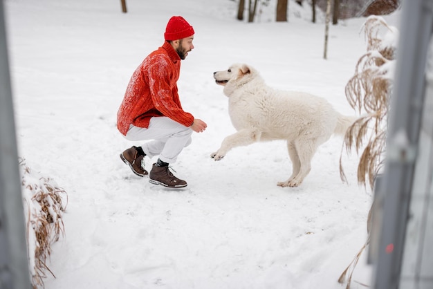 Man in rode trui en hoed speelt met een hond op besneeuwd gazon Samen de winter doorbrengen