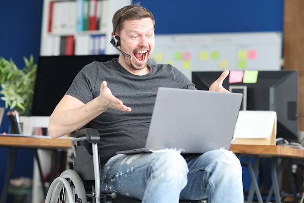 Man in rolstoel in hoofdtelefoon communiceren via laptop. Werk voor gehandicapten concept