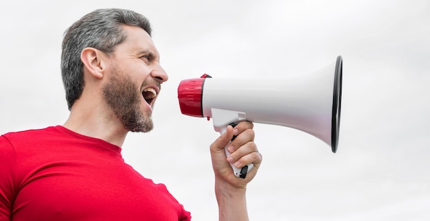 Man in rood shirt schreeuwt in luidspreker op luchtpropaganda als achtergrond