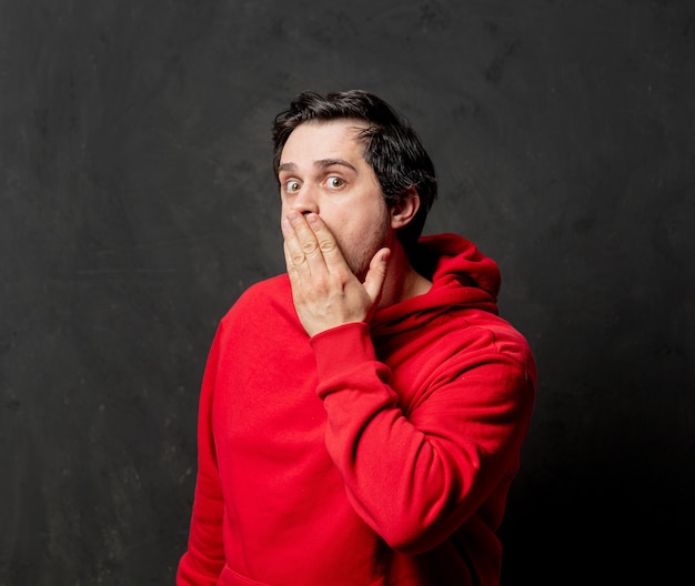 Man in rood sweatshirt toont stil gebaar op donkere muur