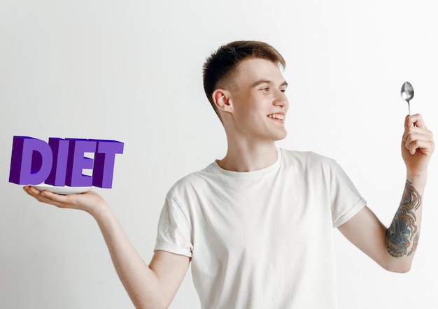 Man in shirt met de folk geïsoleerd op wit. Mannelijk model met een bord met letters van het woord Dieet. Kiezen voor gezond eten, dieet, biologische voeding en een natuurvriendelijke levensstijl.