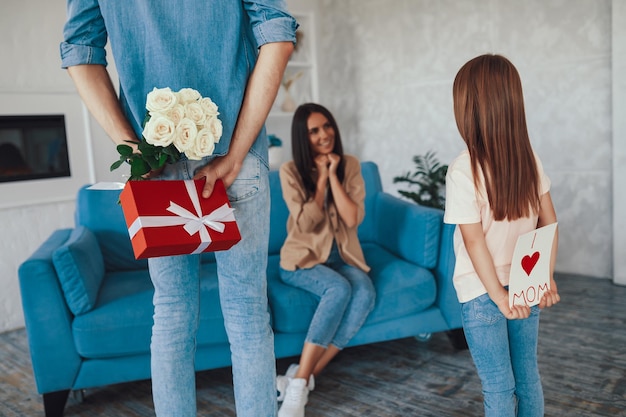 Man in spijkerbroek en zijn dochter die cadeautjes achter hun rug houden en moeder gaan begroeten bij een speciale gelegenheid