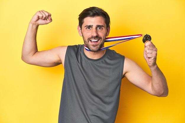 Man in sportkleding die een gouden medaille vasthoudt op een gele studio achtergrond