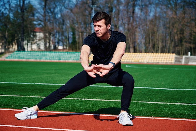 Man in sportkleding doet een warming-up op de stadionbaan voordat hij buiten jogt Gezonde levensstijl