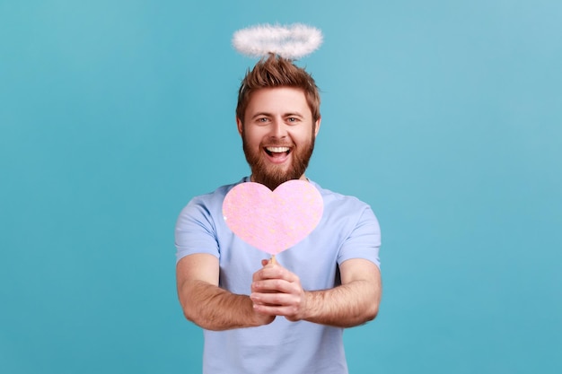 Man in T-shirt met roze papieren hart op stok in handen en toont liefdeszorg romantische gevoelens