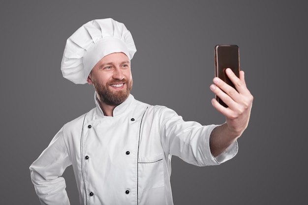 Man in uniform van de chef lacht en neemt selfie