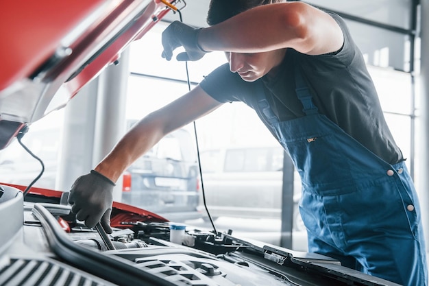 Man in uniform werkt met kapotte auto Conceptie van autoservice