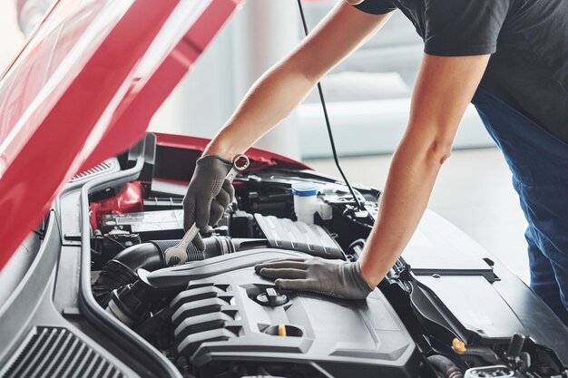 Man in uniform werkt met kapotte auto conceptie van autoservice