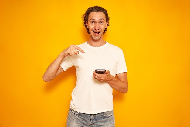 man in vrijetijdskleding wijst met zijn vingers naar smartphone geïsoleerd op gele achtergrond ruimte voor tekst