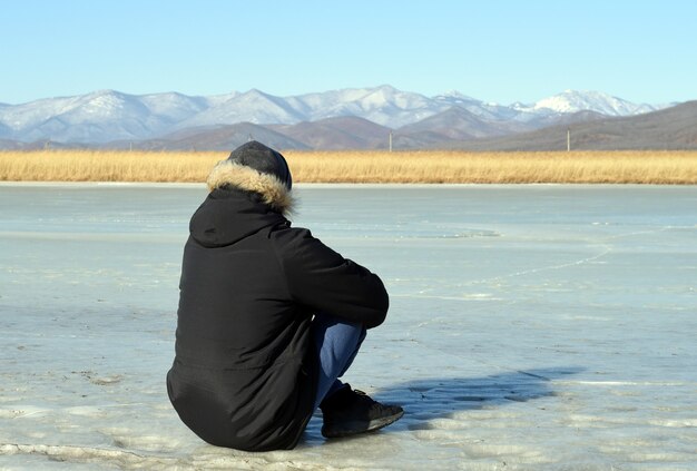 写真 氷の上に座って雪山を見ている暖かい服を着た男