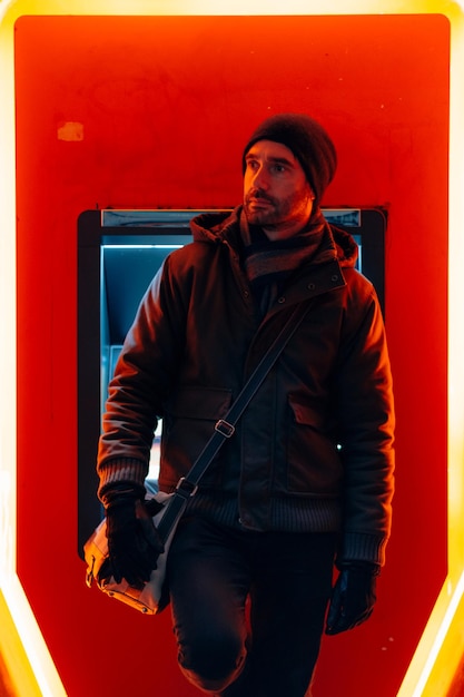 Man in winterkleren met handschoenen en schoudertas die voor een bankautomaat staat
