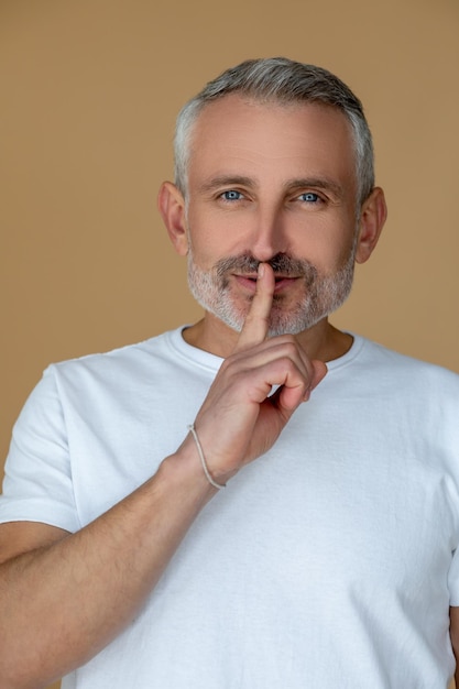 Man in witte t-shirt die een stiltegebaar maakt