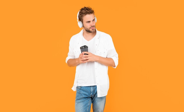 Man in witte t-shirt draagt koptelefoon en houdt koffiekopje op geel modern apparaat als achtergrond