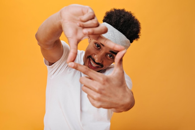 Man in witte tshirt poseren op oranje achtergrond Cool tiener man in sport tee en hoofdband glimlachend op geïsoleerde achtergrond