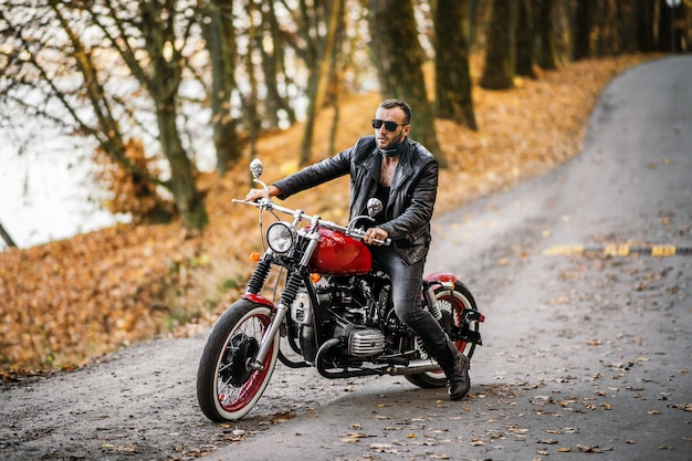 Man in zonnebril en leren jas zittend op een motorfiets op de weg