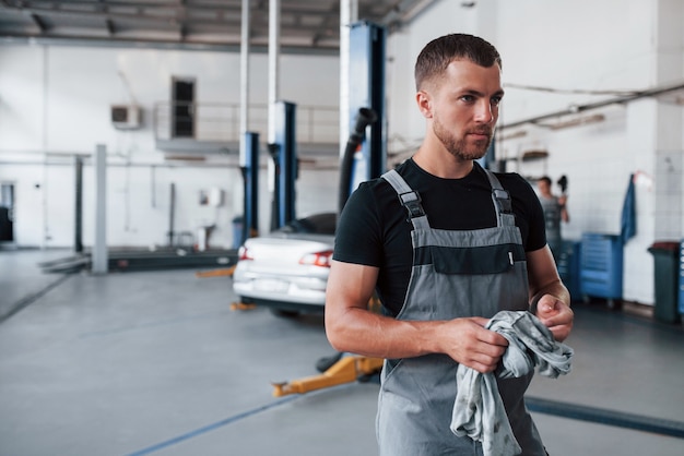 Man in zwart shirt en grijs uniform staat in garage na reparatie van kapotte auto