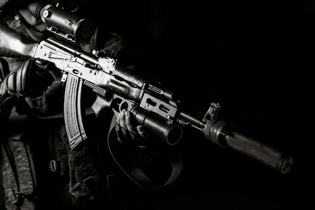 Man in zwart uniform gericht met tot zwijgen gebracht Kalashnikov assault rifle op zwarte achtergrond