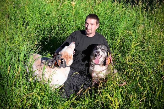 Man in zwarte kleren met twee honden zittend op groen gras.