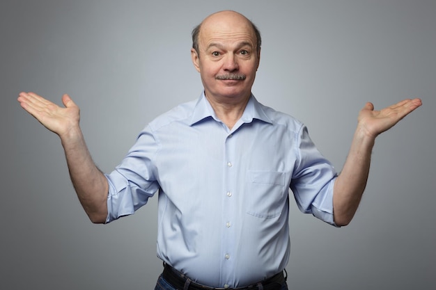 A man in an informal shirt raises his arms to the sides in bewilderment and confusion