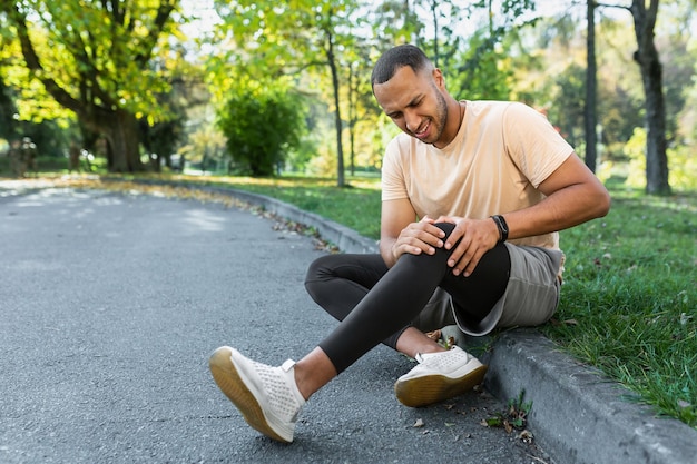 Man injured leg while jogging african american man sitting on ground massaging sore muscle with