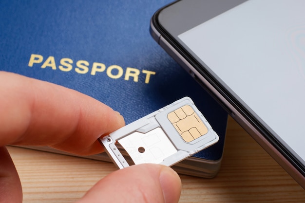 Man inserting tray for SIM card and micro SD memory card to the mobile phone near passport