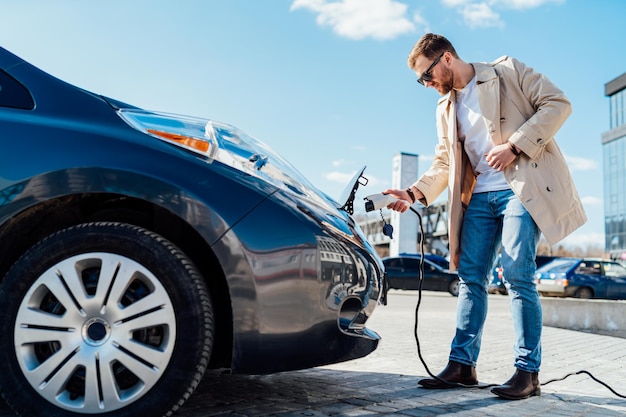 Man inserts the charging cable into the socket of electric car