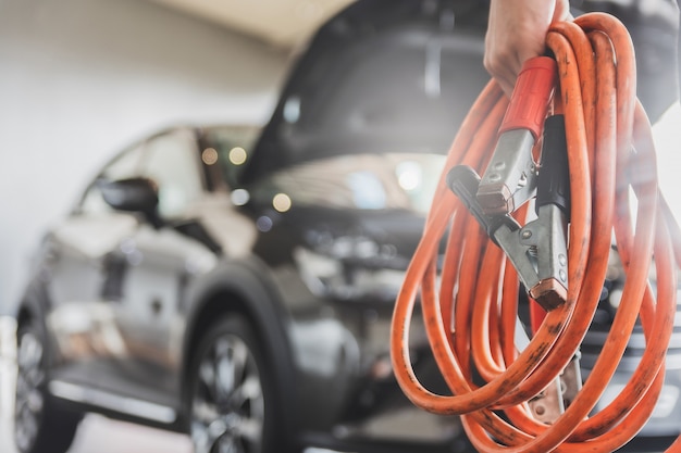 Man inspection holding jumper cables for charger Battery service maintenance of cars