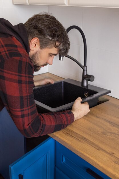 Photo man installing black stone sink into wooden countertop in kitchen vertical