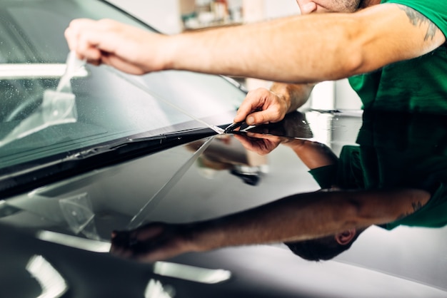 Photo man installs car paint protection film on hood. transparent protective coating against chips and scratches