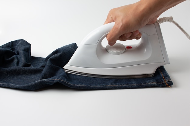 Man ironing blue jeans on white table in the room.