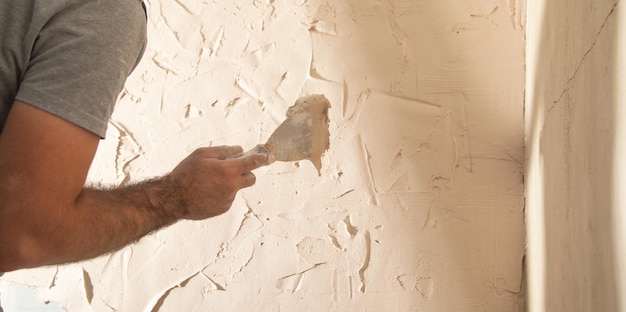 Photo man is applying putty on a wall renovating house