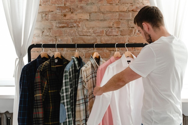 Man is browsing through his various shirts hanging on the clothing rack in the wardrobe