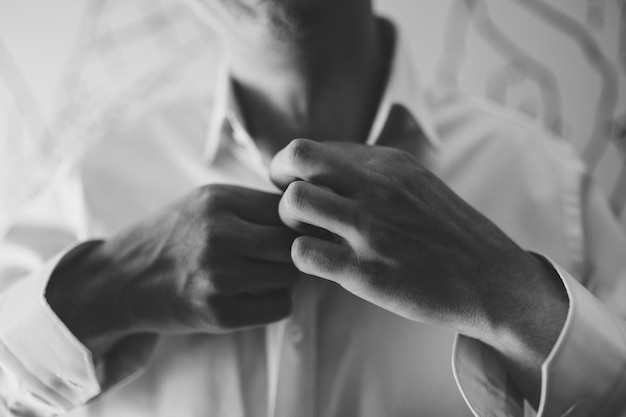 Man is buttoning the buttons on a white shirt closeup black and white photo