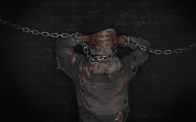 Foto un uomo è incatenato a un muro di mattoni con una catena intorno alla testa.