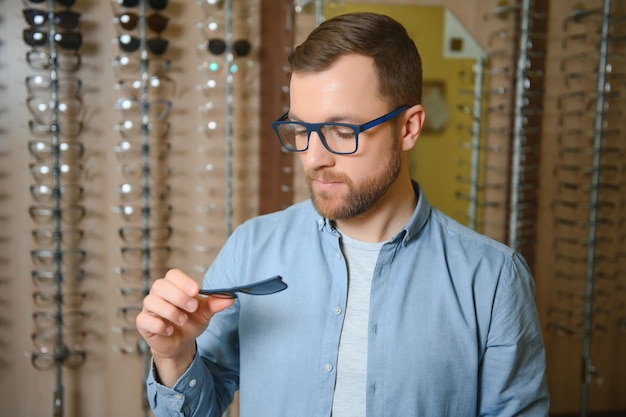 Man is choosing glasses in optics store