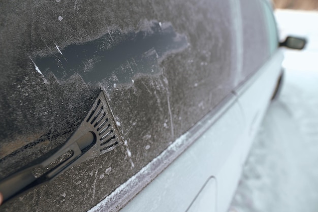 男は氷のスクレーパーで車の凍った窓を掃除しています 寒い雪と霜の降りた朝