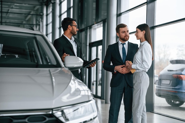 男は車ショールームで若いカップルに相談している