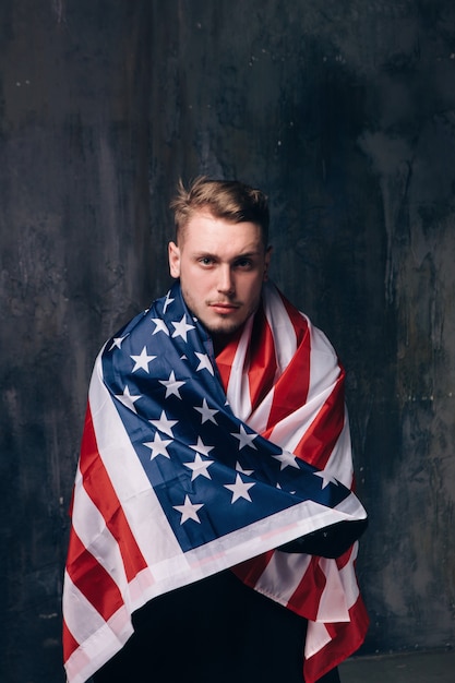 Man is covered by american flag on dark background