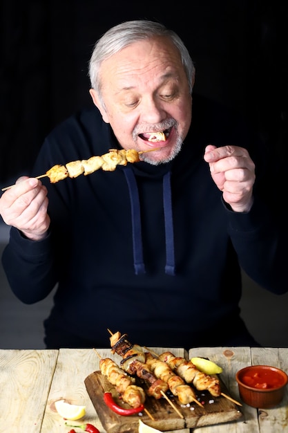 男は鶏の串焼きを食べています