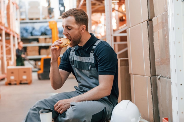 Man is eating lunch Taking a break Employee in uniform is working in the storage at daytime