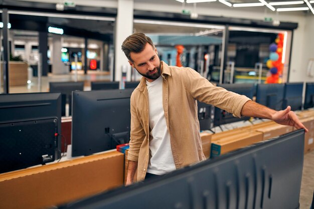 Man is eyeing plasma tv in store of household appliances,
electronics and gadgets. buying new tv, sale day.