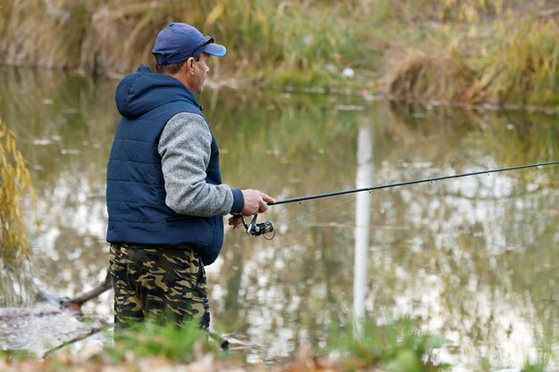 男性が青いベストを着て池で釣りをしています