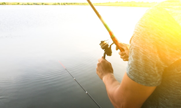 남자는 호수 근처에서 막대로 낚시를 하고 있다. 취미 야외. 기둥으로 자연 속에서 물고기를 잡습니다.