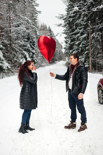 Man is giving heart shaped balloon to his woman both smiling