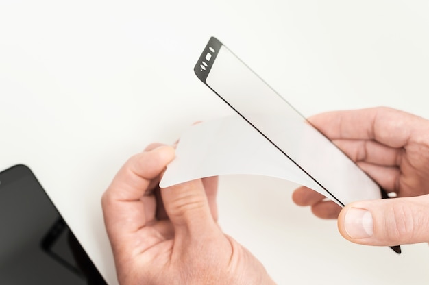 A man is glueing a protective glass on the screen of a smartphone