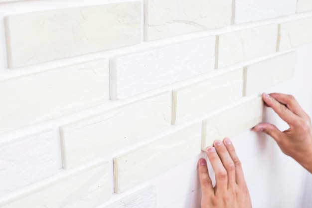 A man is gluing a plaster of white tiles on a wall. Homemade apartment repair